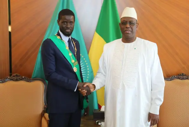 Senegalese President Bassirou Diomaye Faye (left) shakes hands with former President Macky Sall (right) during an official ceremony